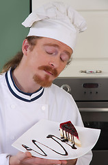 Image showing Funny young chef smelling a piece of cake