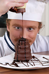 Image showing Funny young chef added chocolate sauce at piece of cake