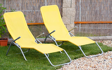 Image showing Two empty yellow sun loungers on a garden 