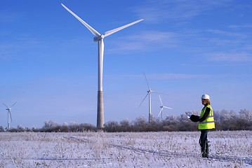 Image showing Young architect-woman wearing winter cloth standing against wind turbines