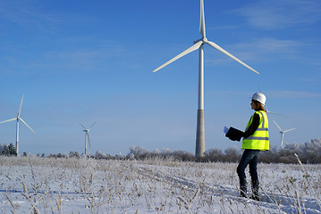 Image showing Young architect-woman wearing winter cloth standing against wind turbines