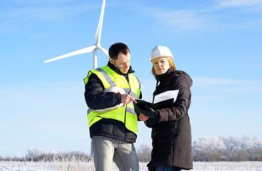 Image showing Young architect-woman wearing winter cloth and engineer standing against wind turbines