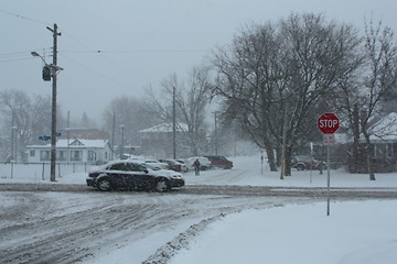 Image showing Picture taken during a winter storm that passed by the city - snow covered a busy intersection - car passing
