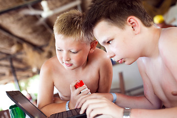 Image showing Two boys play a laptop on rest in a bar on a beach
