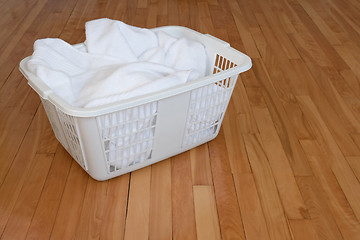 Image showing Laundry basket with white towels on wooden floor