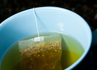 Image showing Green tea brewing in hot water in blue cup