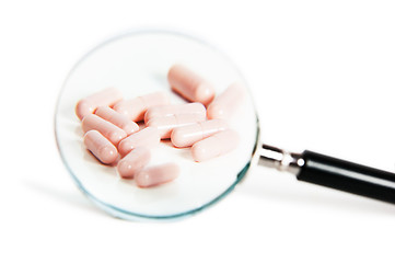 Image showing Group of different pills on magnifying glass. On white backgroun