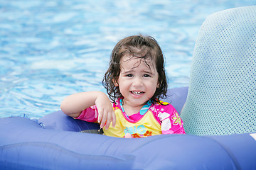 Image showing Baby girl having fun on a blue float into a tropical swimming po