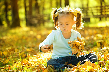 Image showing Cute little girl is playing with leaves in park