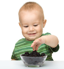 Image showing Cute cheerful little boy is eating blackberry