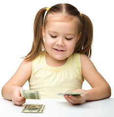 Image showing Cute cheerful little girl is counting dollars