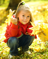 Image showing Cute little girl is playing with leaves in park