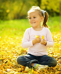 Image showing Cute little girl is playing with leaves in park