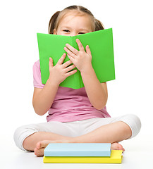 Image showing Cute little girl is hiding behind a book