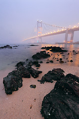 Image showing rocks on the beach and bridge in mist