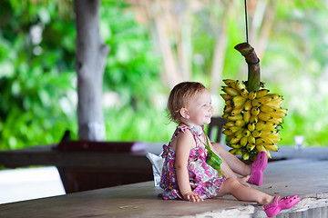 Image showing Toddler girl outdoors with bunch of bananas