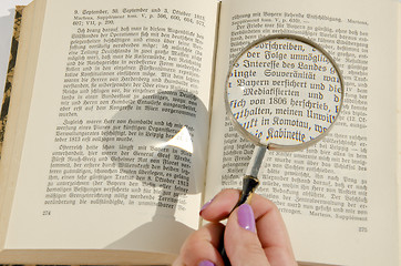 Image showing Woman's hand holding magnifying glass over the german book page. 