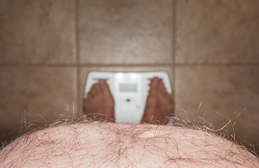 Image showing Hairy man stomach overhangs feet on scales