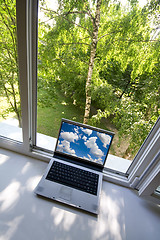 Image showing Opened plastic window in room with view to green trees and portable computer
