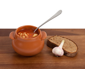 Image showing Soup in clay pot with bread and garlic on wooden table