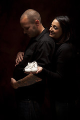 Image showing Mixed Race Couple Holding New White Baby Shoes on Black