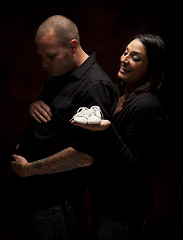 Image showing Mixed Race Couple Holding New White Baby Shoes on Black