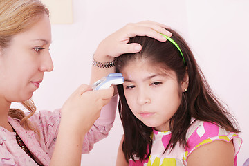 Image showing Portrait of a sick child being checked with a thermometer by a d