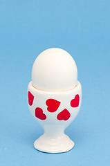 Image showing white egg in special cup eating on blue background 