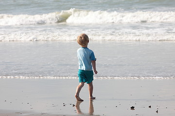 Image showing young child walking on the sand to the waves