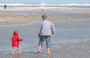 Image showing Grandmother and granddaughter walking on the beach with feet in water