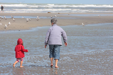 Image showing Grandmother and granddaughter walking on the beach with feet in water