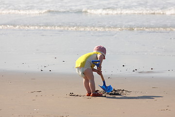 Image showing young child playing with a shovel on the sand of the beach