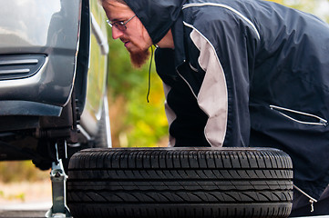 Image showing Young adult inspecting the wheel of a car