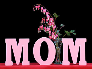 Image showing The word MOM isolated on black with a vase of bleeding hearts.