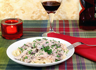 Image showing Beef Stroganoff and egg noodles with wine and a lit candle.