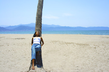 Image showing Young woman leaning on a palm tree