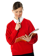 Image showing Cute school girl thinking and looking into notebook