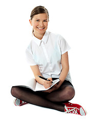 Image showing Charming girl seated on floor with notebook on her lap