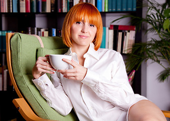 Image showing woman with red hair ist sitting on a chair and drinking coffee