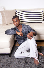 Image showing dark-skinned man sitting on the floor in front of the couch