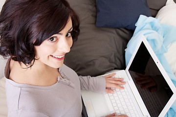 Image showing young beautiful brunette woman is sitting on a sofa with a notebook