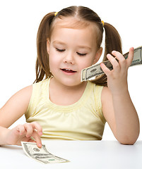 Image showing Cute cheerful little girl is counting dollars