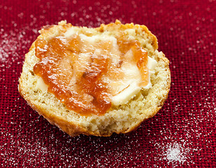 Image showing Half scone with butter and jam on red tablecloth