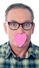 Image showing Surprised aged male with paper heart over his mouth