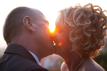 Image showing Bride and groom kissing at sunset