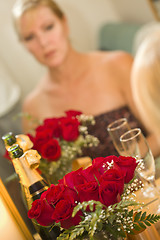 Image showing Pensive Blonde Sits at Mirror Near Champagne and Roses