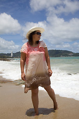 Image showing A woman in a white hat and a pink dress walking on the beach