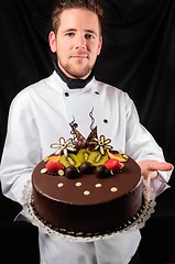 Image showing Handsome chef with cake against dark background