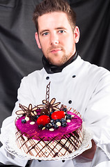 Image showing Handsome confectioner with cake against dark background