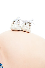 Image showing tummy of pregnant woman with small boots on isolated white